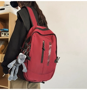 Detail of burgundy student backpack with nylon texture and cute plush monkey charm