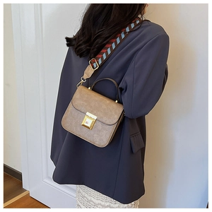 Detail of vintage brown leather bag with colorful wide woven strap worn over a grey blazer