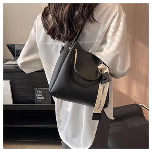 Detail of black leather bucket bag with gold handle and woven fashion strap