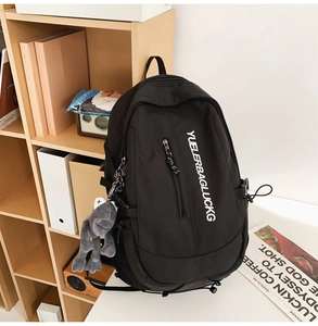 Close-up of black nylon backpack with multi-zipper pockets and grey plush charm