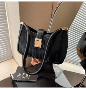 Detail of black textured handbag with gold square buckle and dual straps in a mirror reflection