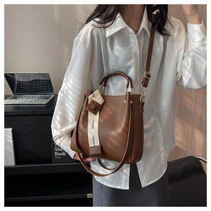 Detail of a dark brown leather bucket bag featuring a cream webbing strap with Fashion text