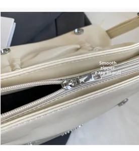 Close-up of smooth silver metal zipper and rivet details on cream leather shoulder bag