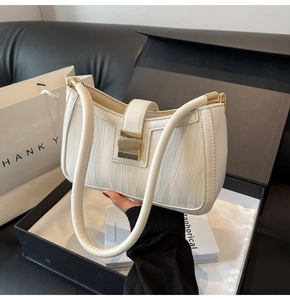 Detailed view of cream textured handbag with gold clasp inside a luxury black gift box