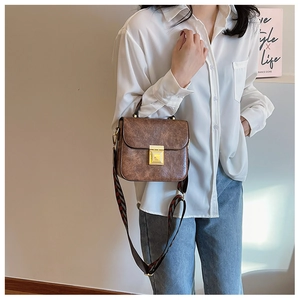 Detail of vintage brown textured crossbody bag with golden clasp and wide striped strap