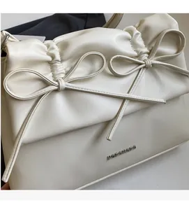 Detailed close-up of cream-white bag with bow decor, pleated texture, and silver logo