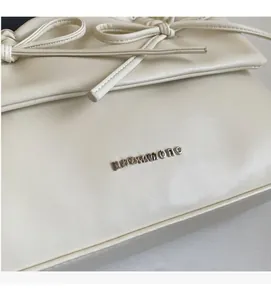 Detail of silver NOROMORO logo and leather bow on an off-white tote bag