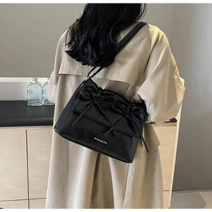 Detail of minimalist black leather tote bag with three decorative bows on windcoat model