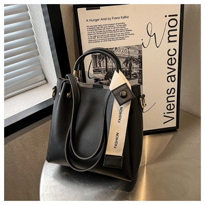 Detail of black matte leather bucket bag featuring a wide FASHION woven shoulder strap