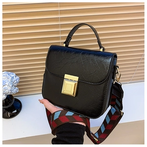 Detail of black vintage textured bag with golden square lock and colorful woven strap