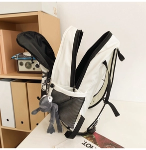 Detailed view of white nylon backpack with black mesh pockets and plush frog charm