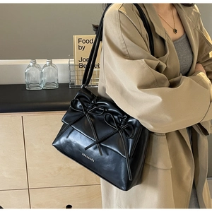 Detail of black glossy PU leather tote bag featuring elegant double bow decoration