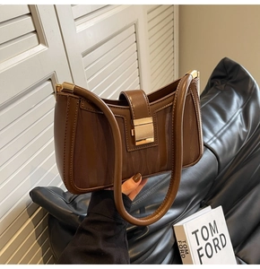Close-up of a brown textured leather handbag with a gold square clasp and stylish handle