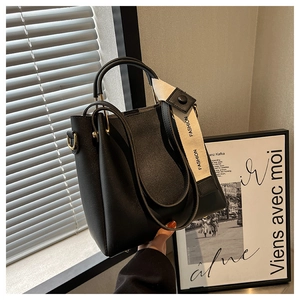 Detail of black leather bucket bag with gold hardware and wide fashion printed strap