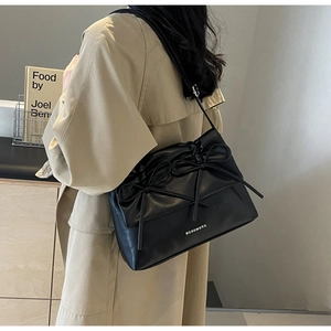 Detailed close-up of black pleated shoulder bag with bow and Noromoro logo on beige coat