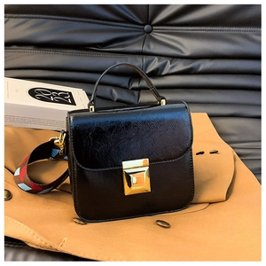 Detail of vintage black oiled leather crossbody bag with gold lock and colorful strap