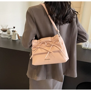 Pale pink leather shoulder bag with bow detail shown in a cozy cafe setting