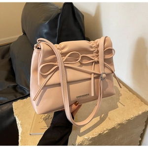 Detail of a light pink leather crossbody bag featuring a bow tie and metal logo