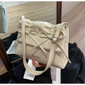 Detail of cream leather shoulder bag featuring ribbon bows and metallic branding logo
