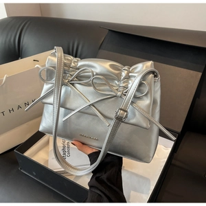 Detail of silver metallic tote bag featuring pleated design and dual bow accents in a gift box