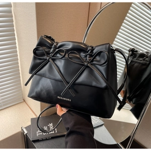 Detail of black leather tote with ribbon bows and metal logo against a mirror reflection