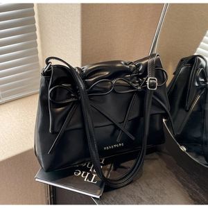 Detail of black pleated PU bag with leather bow and golden logo reflected in a side mirror