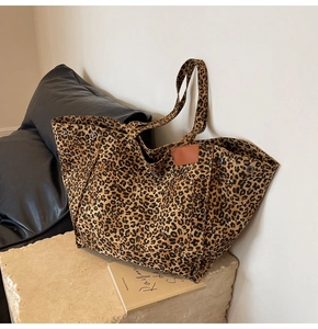 Detail of leopard print tote bag with leather logo patch and metal rivets on stone