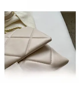 Close-up of quilted beige crossbody bag with gold chain strap and turn-lock closure