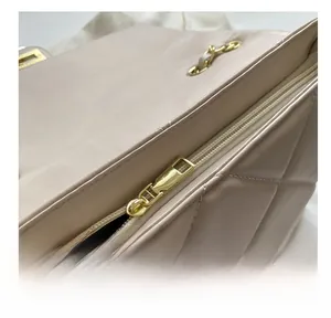 Close-up of smooth gold zipper and quilted diamond pattern on beige shoulder bag