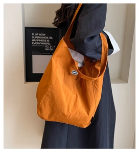 Detail shot of the durable orange tote bag fabric and small oval logo patch on side