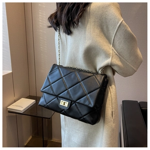 Detail of black quilted leather shoulder bag with gold chain strap on beige coat