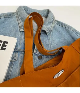 Close-up of deep orange nylon tote bag with DOUGU logo on blue denim jacket