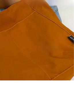 Detail of orange nylon fabric with visible stitching and DOUGU logo on a tote bag