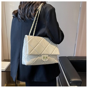 Close-up of beige quilted chain bag with gold metal lock on a model shoulder