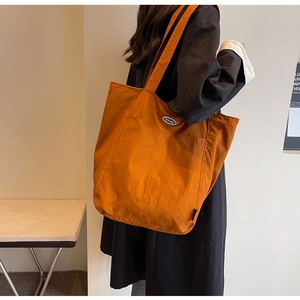 Detail of a large orange tote bag featuring two front pockets and an oval logo label