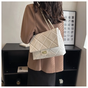 Detailed view of white quilted crossbody bag with gold chain strap on a brown blazer
