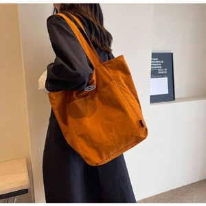 Detail of orange high-capacity tote bag featuring a textured waterproof fabric and logo