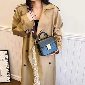 Black leather crossbody bag with geometric woven strap on a model wearing a khaki trench coat