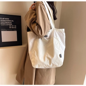 Detailed view of white canvas tote bag with front pocket shown on a shoulder