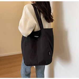 Detail of black canvas tote bag showing the side brand label and metal logo on strap