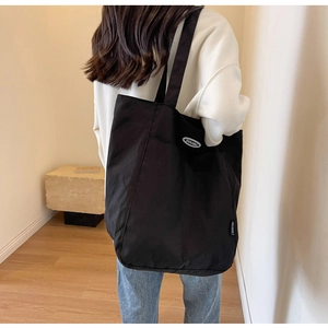 Detail of large black canvas tote bag with DOUGU logo patch and textured fabric finish