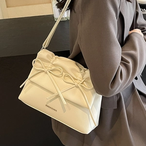 Chic beige tote bag with bow detail and adjustable shoulder strap shown on a model