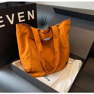 Detail of bright orange tote bag with oval logo patch placed in a premium gift box