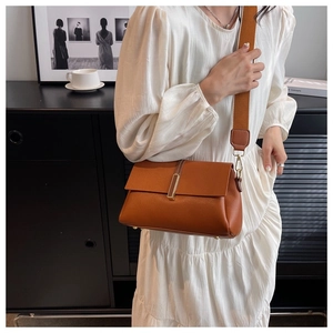 Detail of a brown lychee grain leather crossbody bag with a wide strap and gold clasp