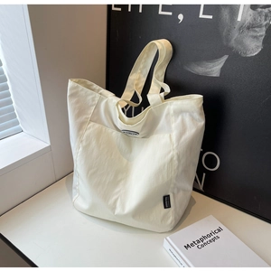 Minimalist cream tote bag detail showing black brand label and oval emblem decoration