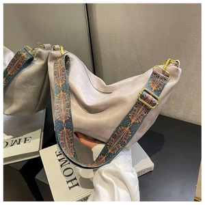 Close-up of beige hobo bag with patterned wide strap and gold hardware on home decor books