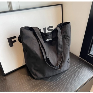 Detail of high-capacity black tote bag with tech nylon texture and DOYGU brand leather label