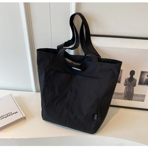 Detail view of the black canvas tote bag with front pocket and woven label on a white desk
