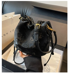 Detail of black bucket bag with golden buckle and oval logo plate on a gift box