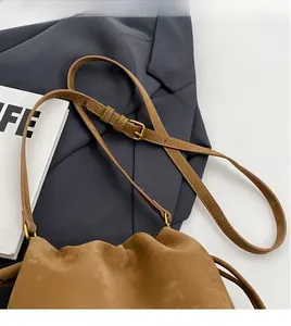 Detail of adjustable shoulder strap and retro gold hardware on brown matte bucket bag